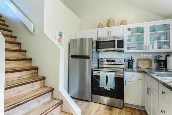 Una cocina moderna con electrodomésticos de acero inoxidable, escaleras de madera y armarios blancos.