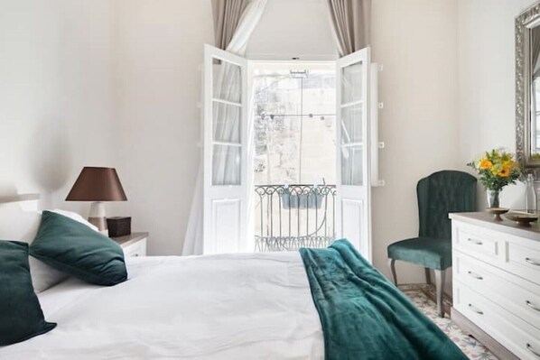 A bedroom with a bed, a nightstand, a dresser, a chair, and a window with curtains. - Historic Maltese Townhouse (Rabat)