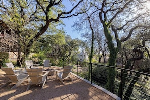 An outdoor seating area with Adirondack chairs and a table, surrounded by trees and a metal railing.