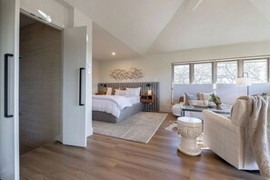 Une chambre moderne avec un grand lit, des tables de chevet et une vue sur l’extérieur grâce à de grandes fenêtres.