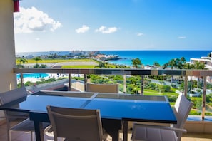 Un balcón con mesa y sillas que da a vistas de la costa, con edificios y vegetación.