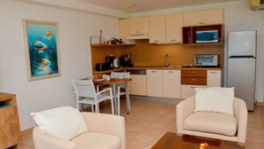 Un espace de vie compact comprenant un coin cuisine, deux canapés, une table à manger et un tableau représentant une scène sous-marine.