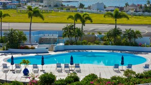 Une piscine entourée de palmiers, avec des chaises longues et des parasols, offrant une vue sur la mer.