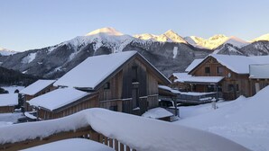 Una cabaña de madera con techos nevados y montañas al fondo.