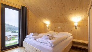 Una habitación de madera con una cama, dos lámparas de noche y vistas a través de un ventanal.