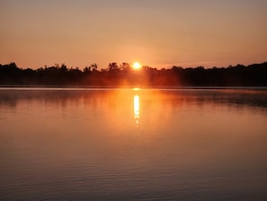 Un lago calmo all'alba, con il sole che si riflette sull'acqua.