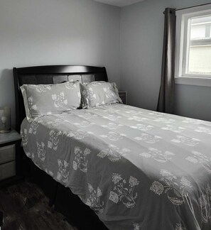 A neatly made bed with a floral-patterned bedspread, a dark wooden headboard, and a bedside table with a lamp. - Escape the city to this quiet home along the beautiful Ottawa River (Westmeath)