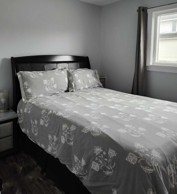 A neatly made bed with a floral-patterned bedspread, a dark wooden headboard, and a bedside table with a lamp.
