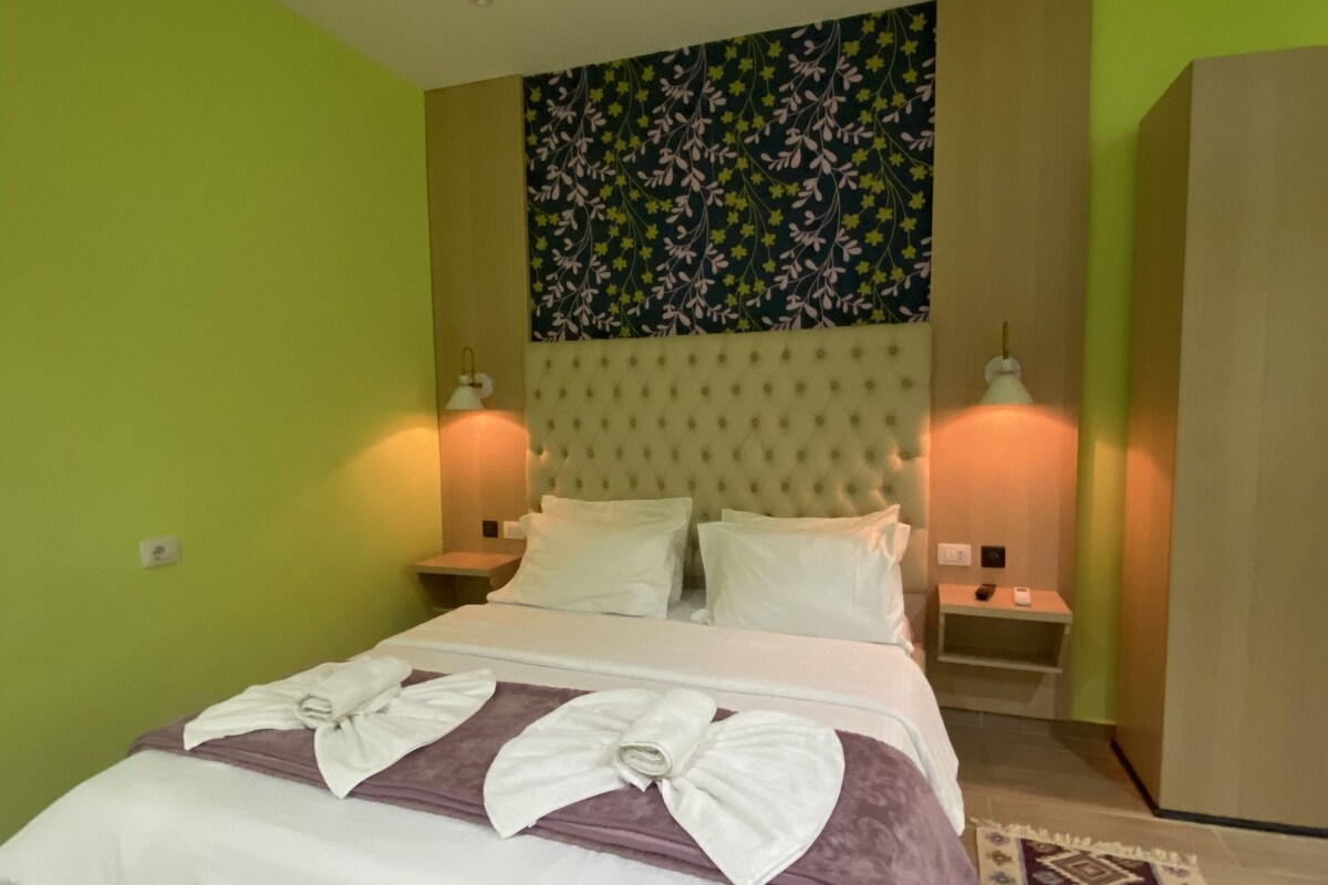 Une chambre d’hôtel avec un lit, deux lampes de chevet, une tête de lit ornée d’un motif floral et un mur vert.