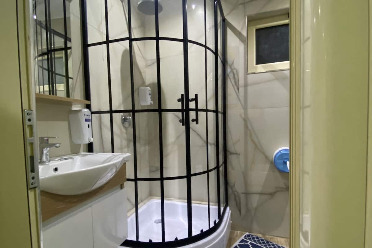 Un baño moderno con ducha de vidrio, lavamanos y un tapete azul estampado en el suelo.