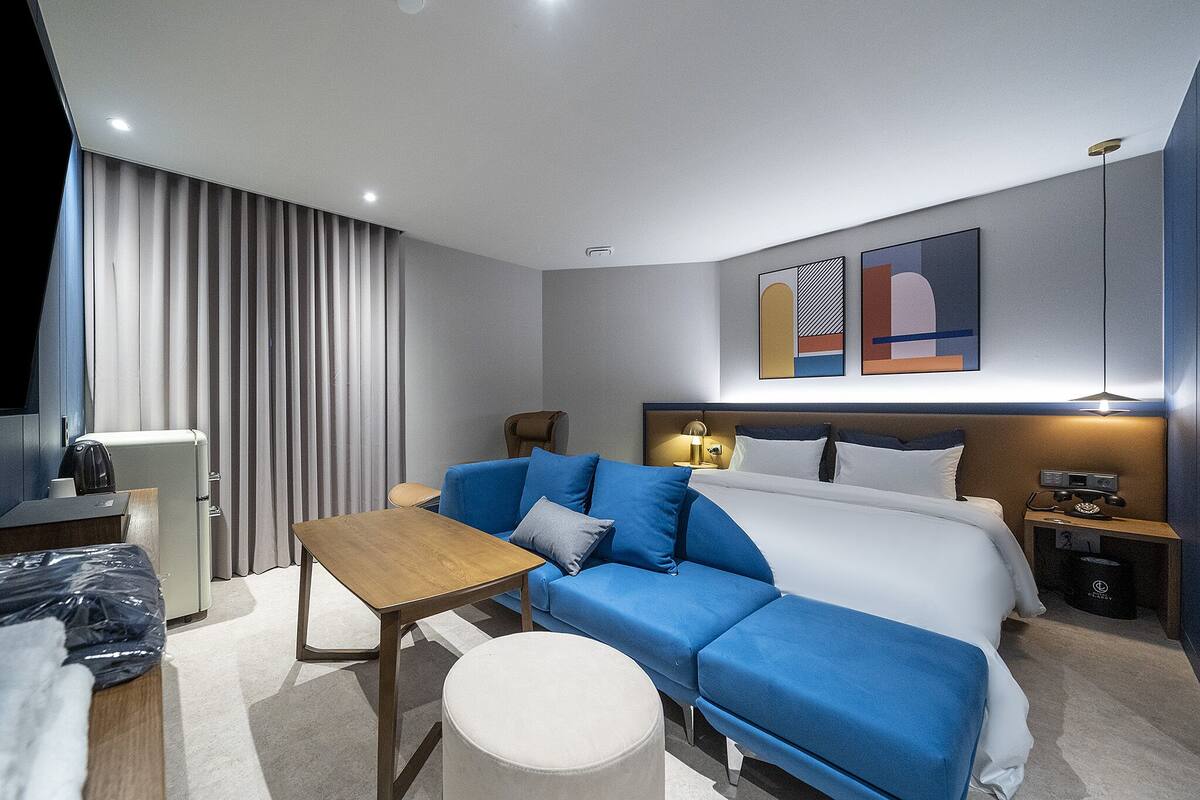 A modern hotel room with a bed, a sofa, a table, and a desk.