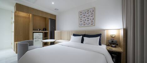A modern hotel room with a large bed, a desk, a chair, and a wardrobe.