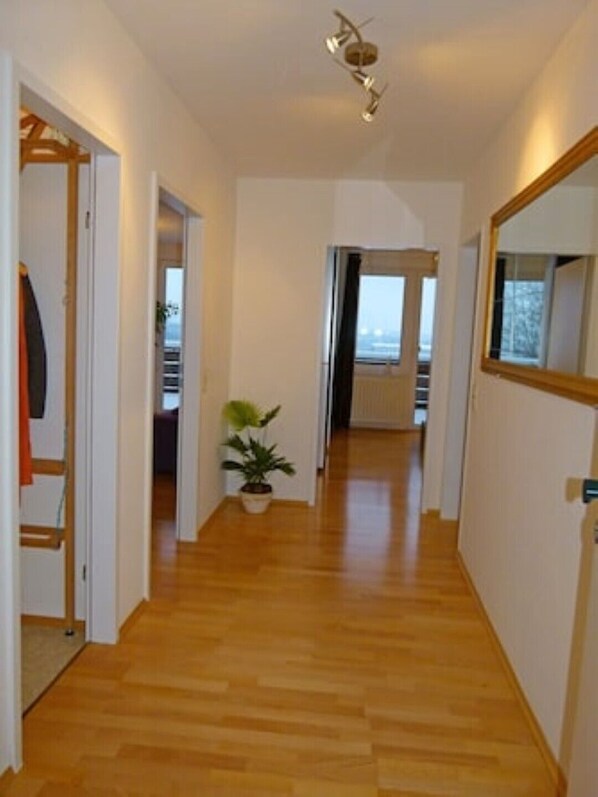 A hallway with wooden flooring, a potted plant, and a mirror on the right wall.