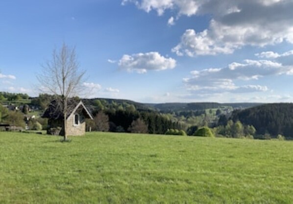 A rural landscape with a small stone building, open fields, and a hilly backdrop.