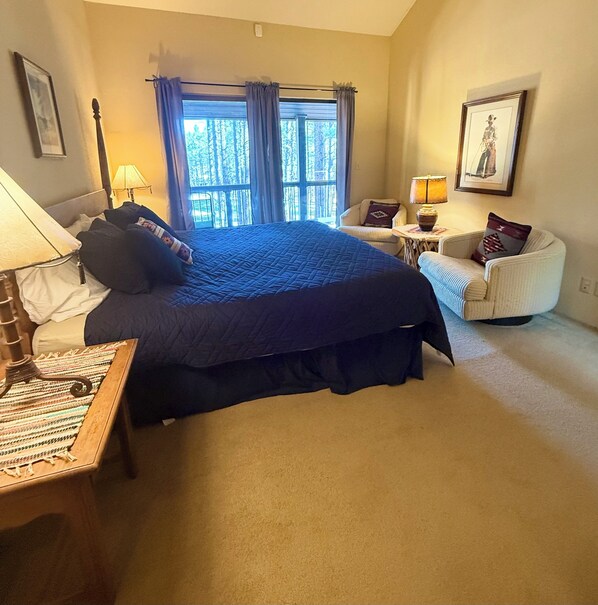 A bedroom with a large bed, a chair, a table, and a window with curtains. - Beautiful, Huge Home on Golf Course and close to Ski Resort. Recently Renovated! (Angel Fire)