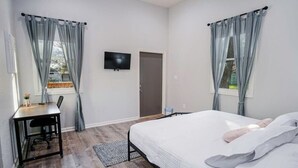 Un dormitorio con cama, escritorio, silla, televisor y puerta.