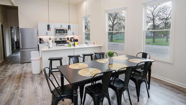 Una cocina moderna con armarios blancos, una isla central y un comedor con una mesa grande y sillas.