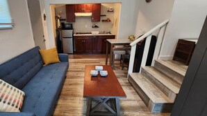 Un espacio habitable compacto con un sofá, una mesita y una escalera que sube a un nivel superior.