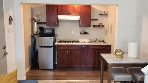 Cocina compacta con armarios de madera, microondas integrado, refrigerador, estufa a gas y encimera de mármol.
