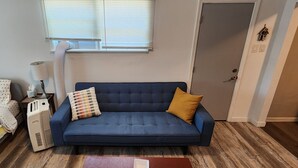 Una habitación con un sofá azul, una mesita con una lámpara, un calentador y una puerta con un detalle decorativo.