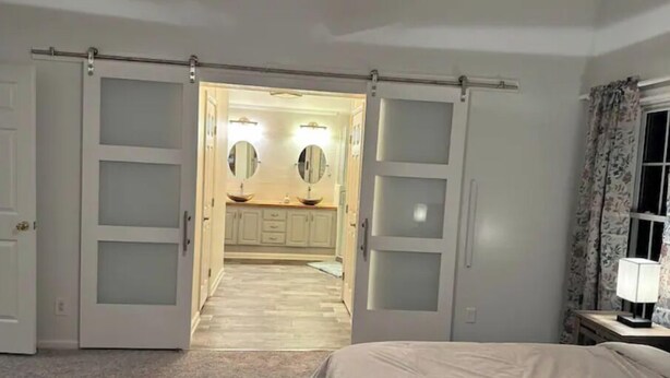 Ein Schlafzimmer mit Bett, Nachttisch, Lampe und einem Badezimmer mit Waschbecken und Spiegel.