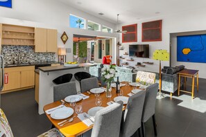 A modern kitchen with wooden cabinets, a dining area with a round table, grey chairs, and a large island with a sink.