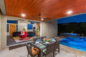 Un espace repas extérieur avec une piscine, un ventilateur de plafond et un intérieur moderne comprenant un canapé et une cuisine.