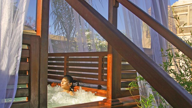 A person in a wooden bathtub with a view of trees and a building in the background. - Riad Flam & Spa (Marrakech)