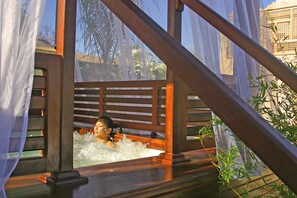 A person in a wooden bathtub with a view of trees and a building in the background. - Riad Flam & Spa (Marrakech)
