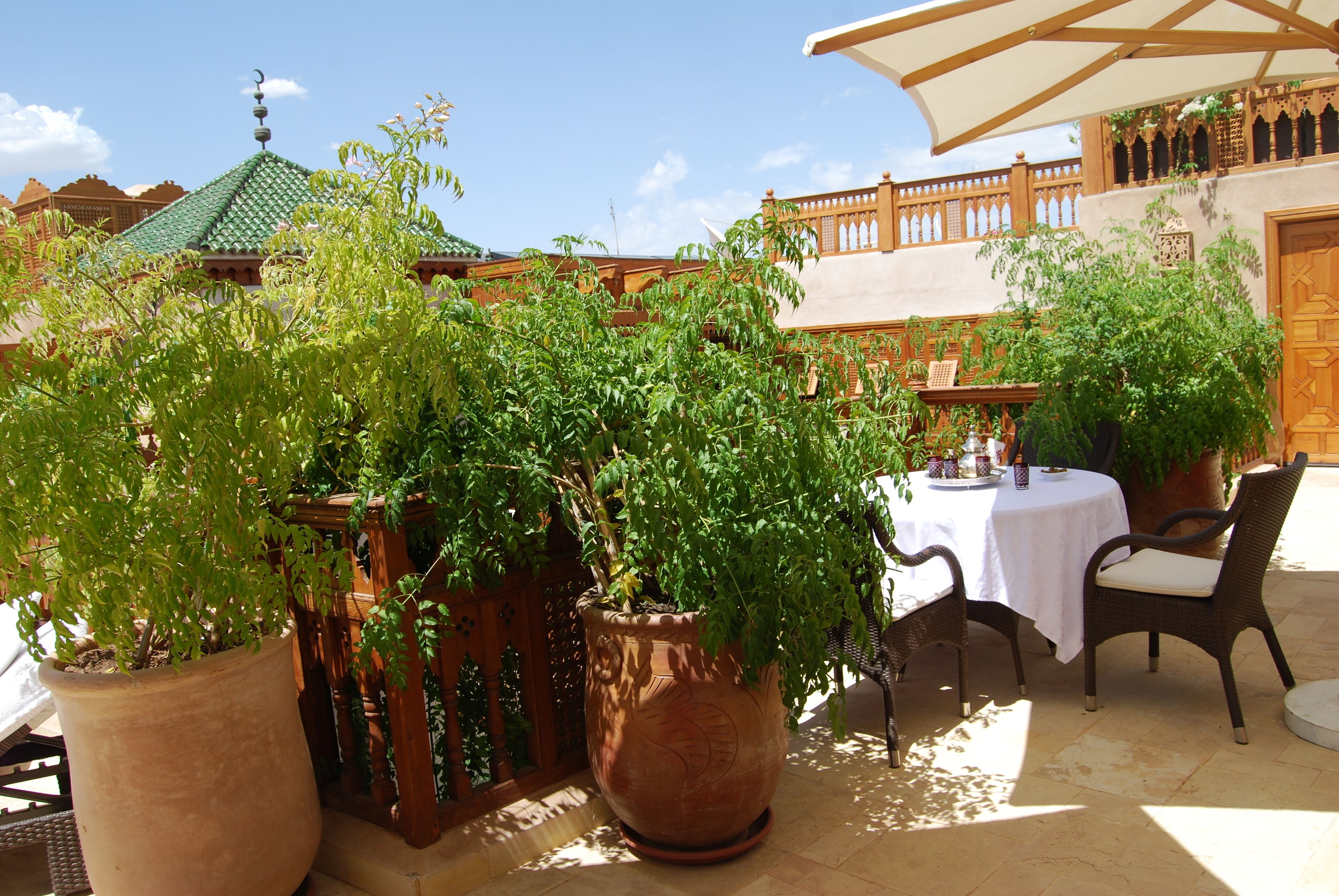 Une terrasse extérieure agrémentée de grands pots en terre cuite, de chaises en osier et d’une table recouverte d’une nappe blanche.