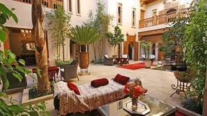 A courtyard with a sofa, chairs, and a table with a vase of flowers. There are potted plants and a tree in the center. - Riad Flam & Spa (Marrakech)