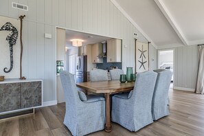 Ein Essbereich mit einem Holztisch und vier gepolsterten Stühlen, im Hintergrund eine Küche und maritime Dekoration, darunter eine Kordel und ein Seestern an der Wand.