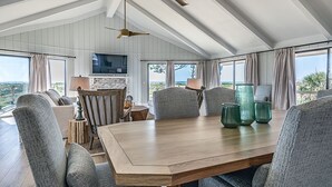 A spacious dining area with a wooden table, grey upholstered chairs, and a television mounted on the wall.