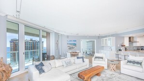 Un salón amplio con un sofá blanco grande, una mesa de centro de madera y vistas al océano a través de ventanales del suelo al techo.