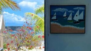 A room with a view of the ocean and sailboats, a palm tree, and a painting of sailboats on the wall. - Villa Kaiae (The Valley)