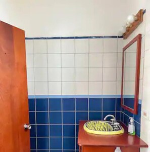 Um banheiro com porta de madeira, pia com cuba amarela, espelho e azulejos azuis e brancos.