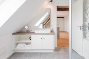 Une salle de bain moderne avec un puits de lumière, un meuble-lavabo blanc et un grand miroir.