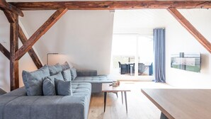 Un loft moderno con vigas de madera a la vista, un sofá seccional gris, una mesa de centro de madera y un ventanal con vistas a la ciudad.
