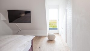 Un dormitorio con cama, televisión instalada en la pared, ventana y puerta que da a un espacio exterior.