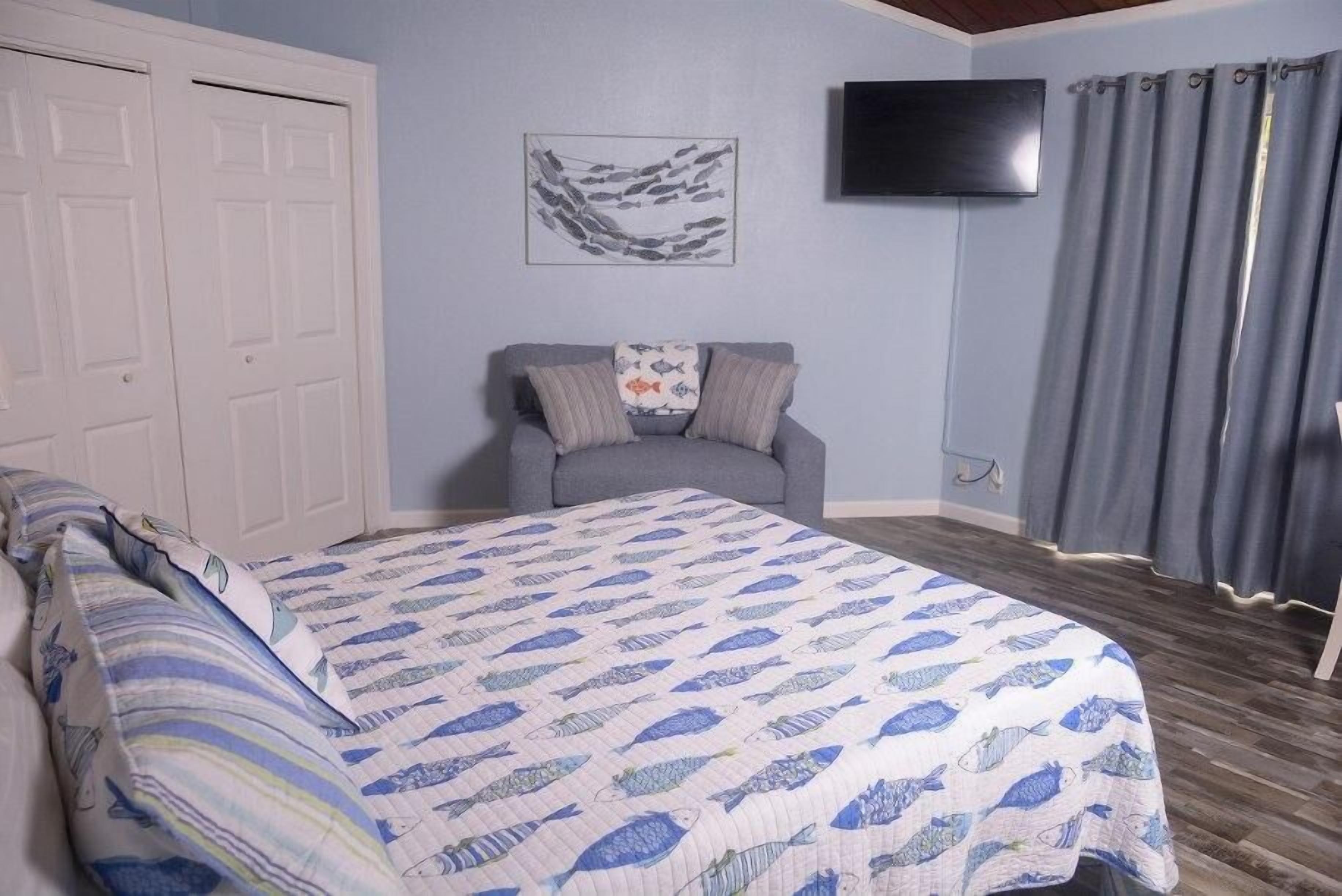 Ein Schlafzimmer mit einem Bett, einem grauen Sofa, einem Flachbildfernseher und einem Bild an der Wand.
