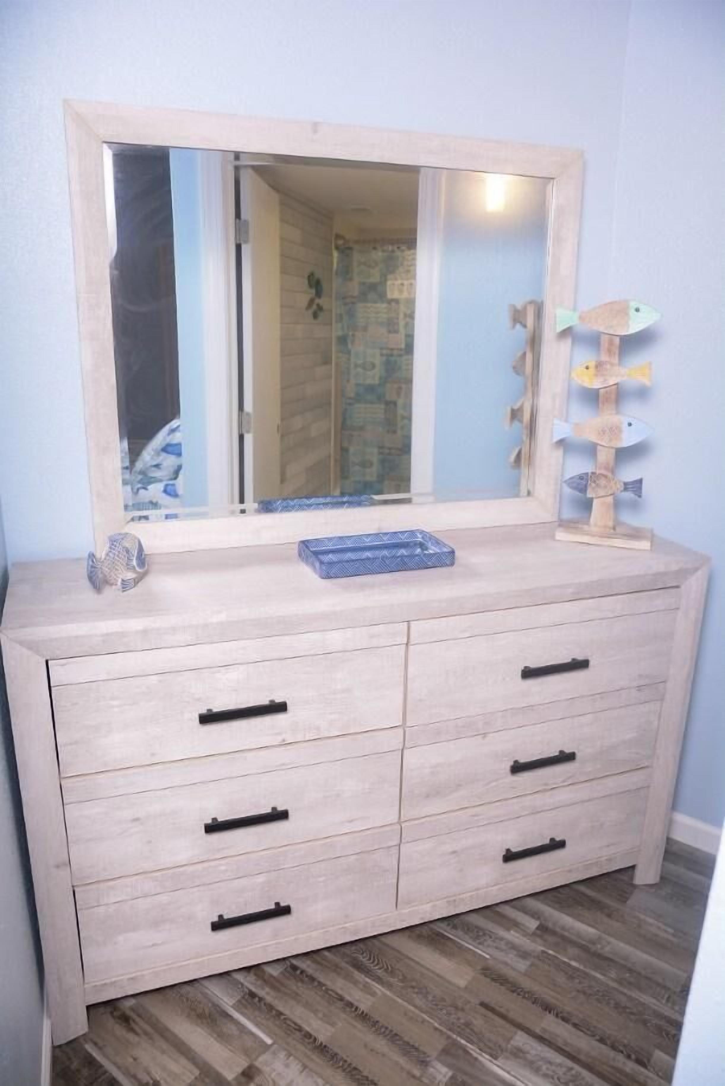 Une commode en bois avec un miroir, des tiroirs et une petite étagère ornée d’objets décoratifs.