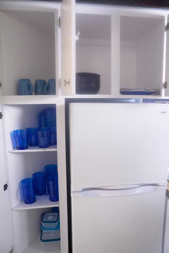 Een witte koelkast met vriesvak, omringd door witte kasten met blauwe opbergdozen.
