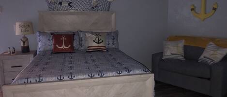 A bedroom with a bed featuring anchor-themed bedding, a grey sofa, and a wall-mounted anchor decoration.