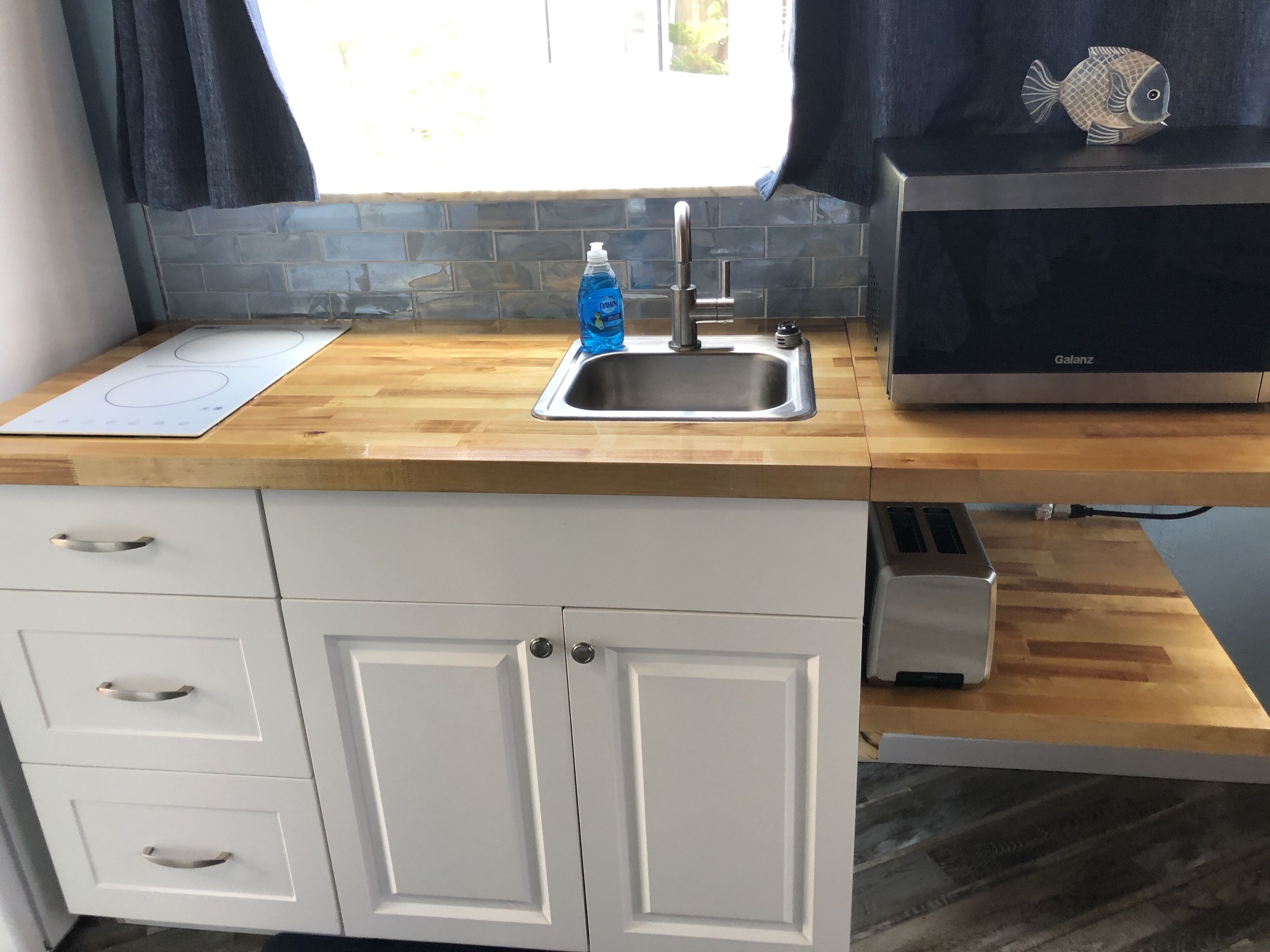 A kitchen with a wooden countertop, a built-in sink, a Galanz microwave, and a white cabinet with drawers.