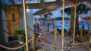 Un área de piscina con una barrera de cuerda, palmeras y una estatua tiki.