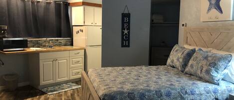 A compact bedroom with a bed, a nightstand, and a wall-mounted shelf.