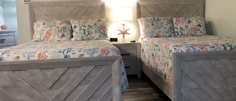 A bedroom with two beds, each with floral bedding and a wooden headboard. There is a nightstand with a starfish decoration and a clock displaying 3:57.
