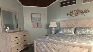 Un dormitorio con una cama de madera, un aparador, un espejo, una decoración de estrella de mar en la pared y un cuadro de un velero.