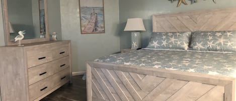 Une chambre à coucher avec un lit en bois, une commode, un miroir, une décoration murale en forme d’étoile de mer et un tableau représentant un voilier.