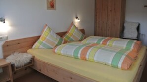 Quarto individual com uma cama de madeira, colchão amarelo e almofadas listradas.